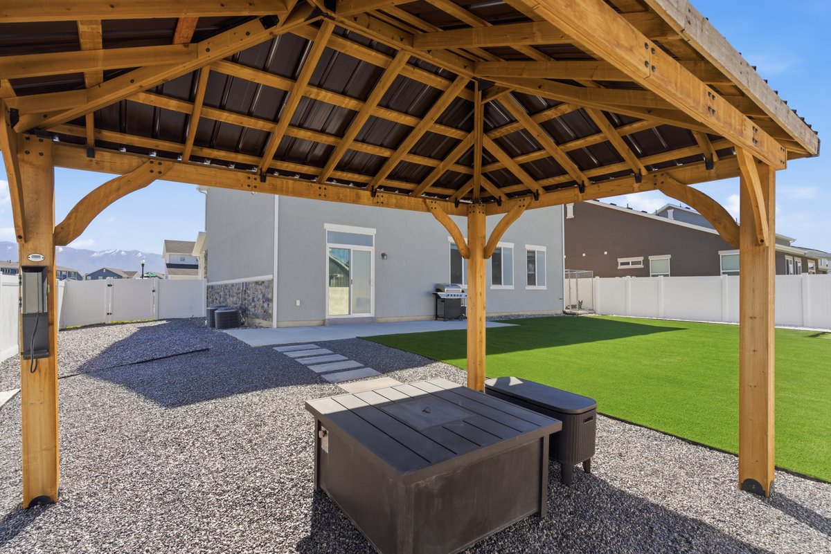 Spacious backyard featuring a wood gazebo with a metal roof, a gravel patio, and artificial turf