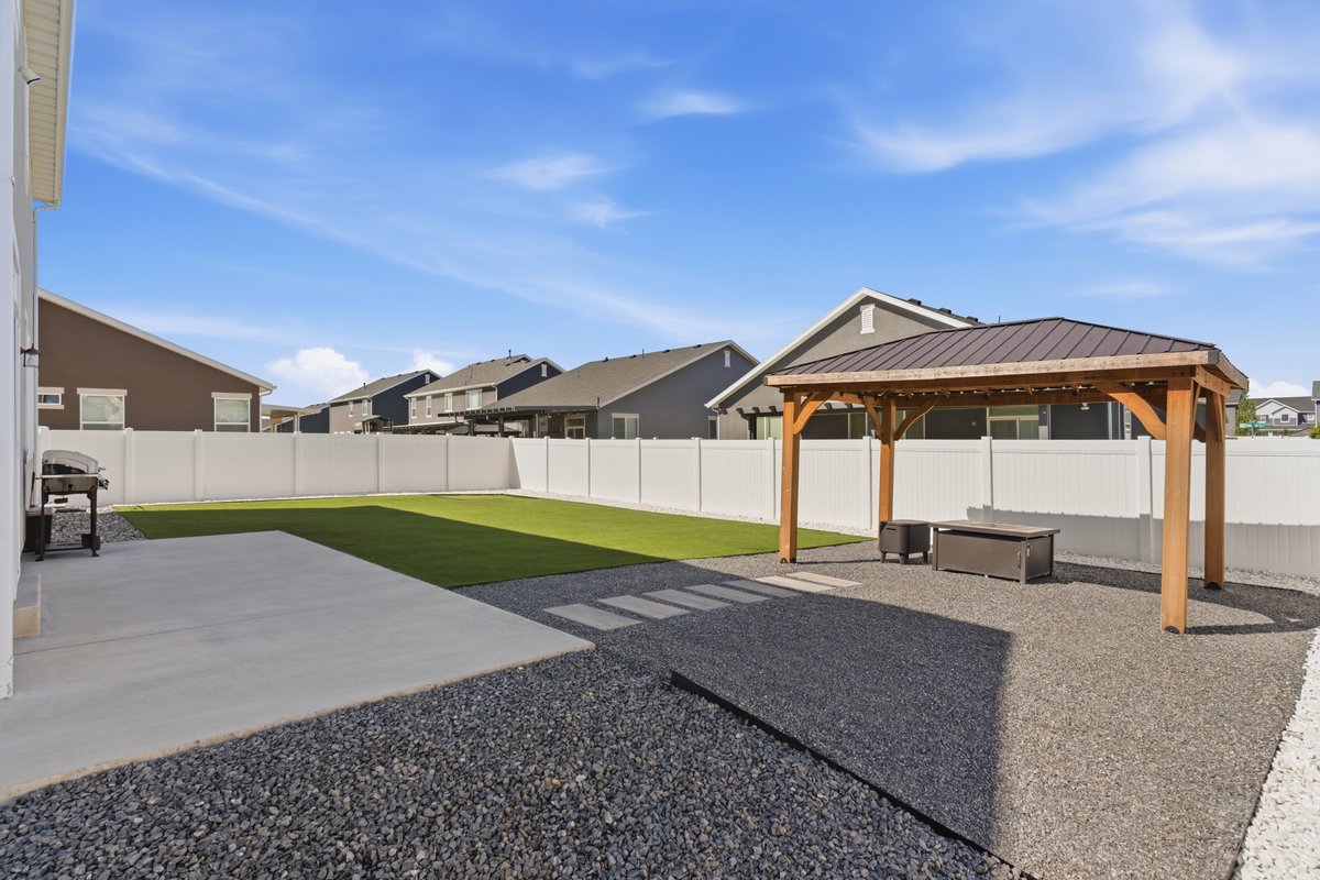 Spacious backyard featuring a large concrete patio, artificial turf, and a wood-frame gazebo with a metal roof