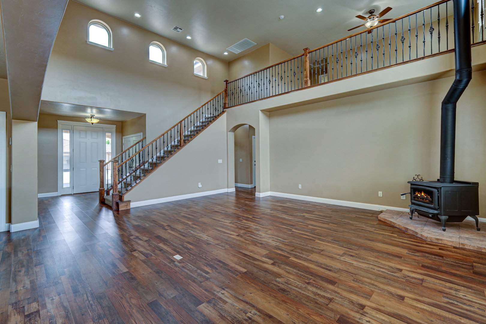 Spacious living area featuring wood-finish flooring, a wood-burning stove with a stone hearth, and a grand staircase with wrought iron balusters