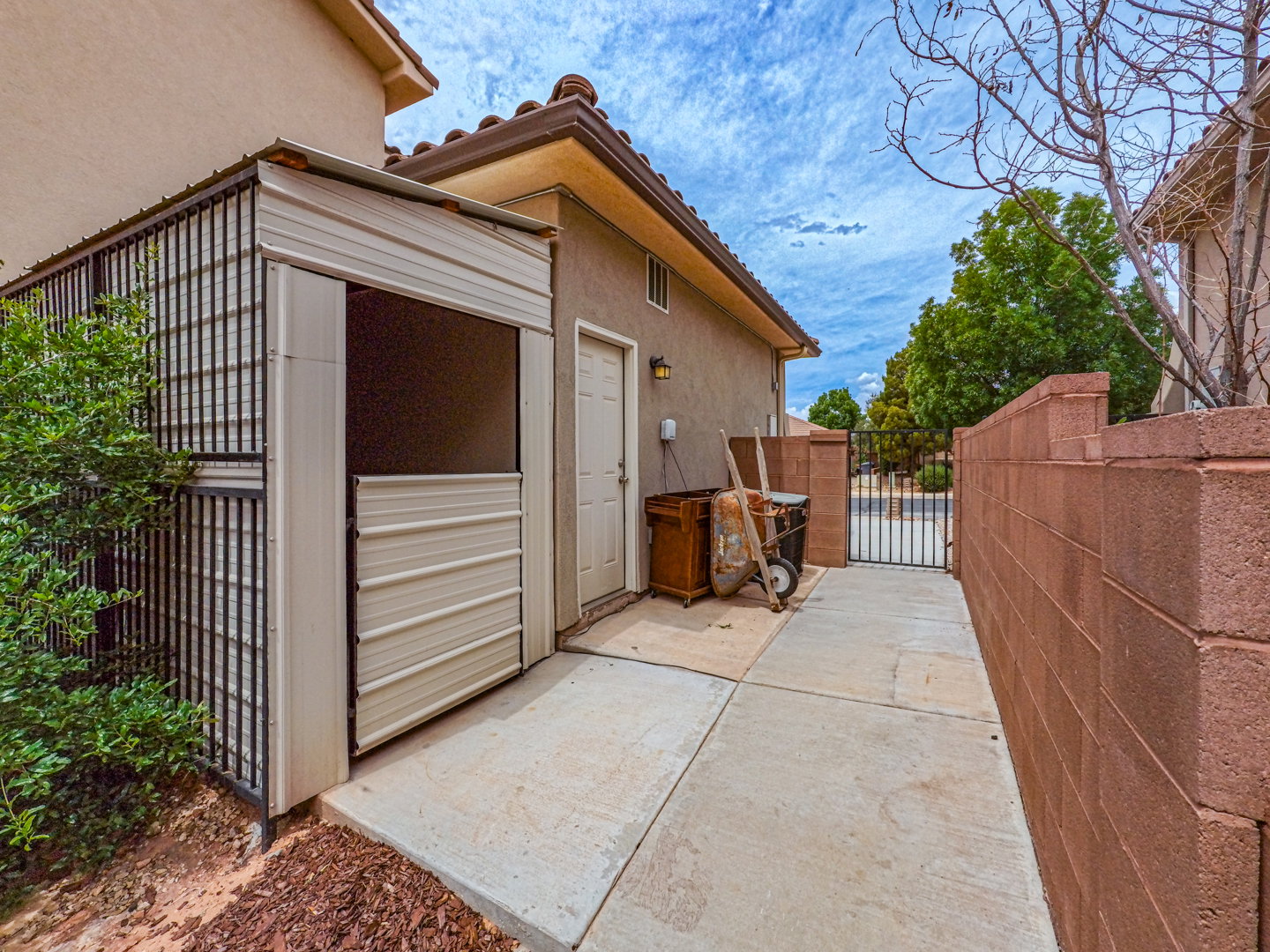 Exterior side yard featuring a concrete pathway, a privacy wall constructed from red cinder blocks, and a metal security gate