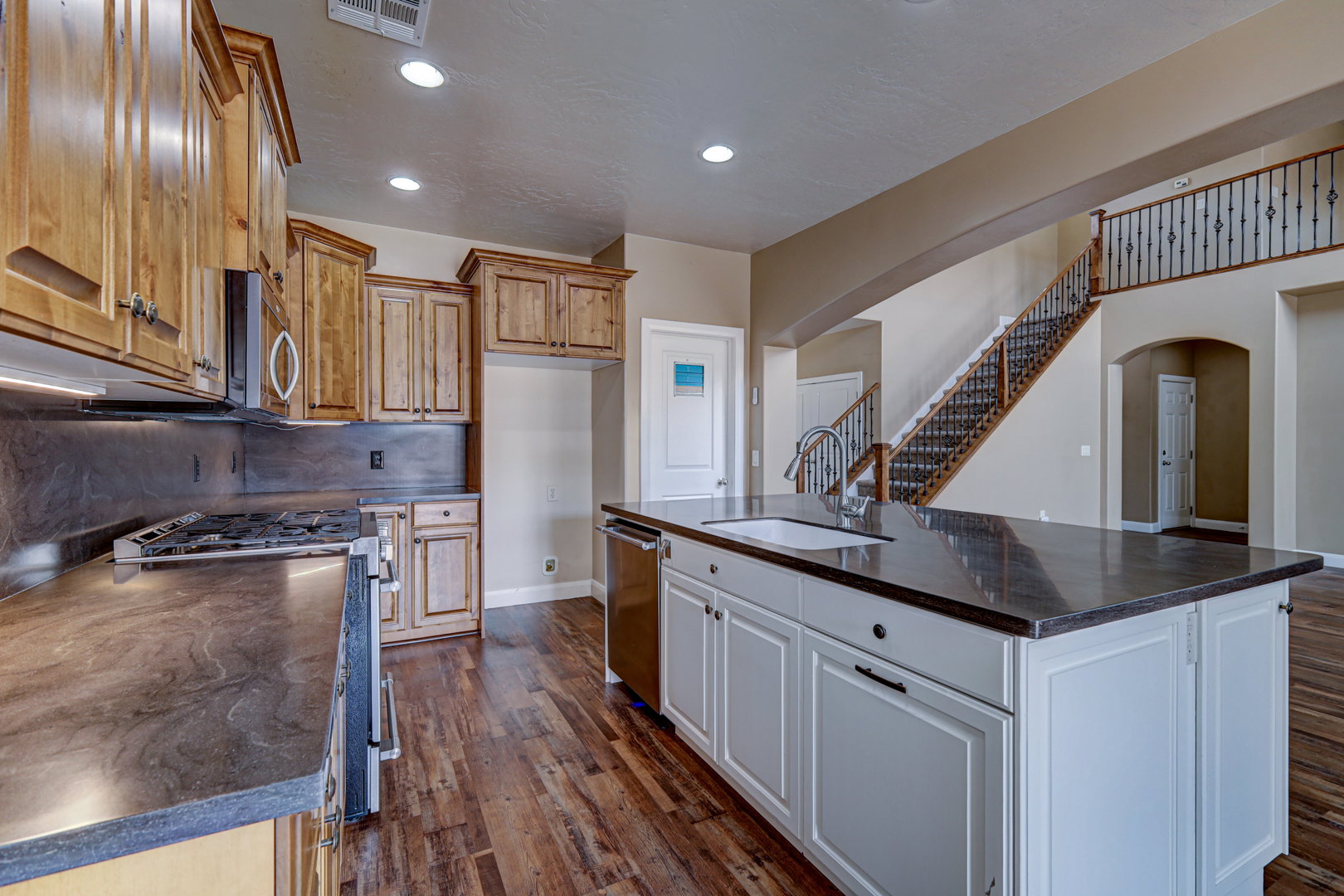 Open-concept kitchen featuring wood-finish flooring, a central island with an undermount sink, dark countertops, and stainless steel appliances