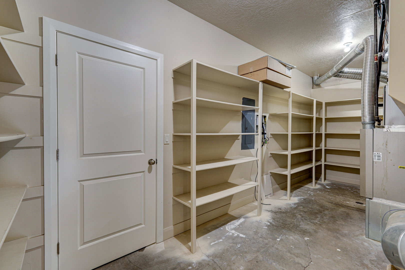 Storage area featuring built-in shelving, a concrete floor, painted drywall, and a white paneled door