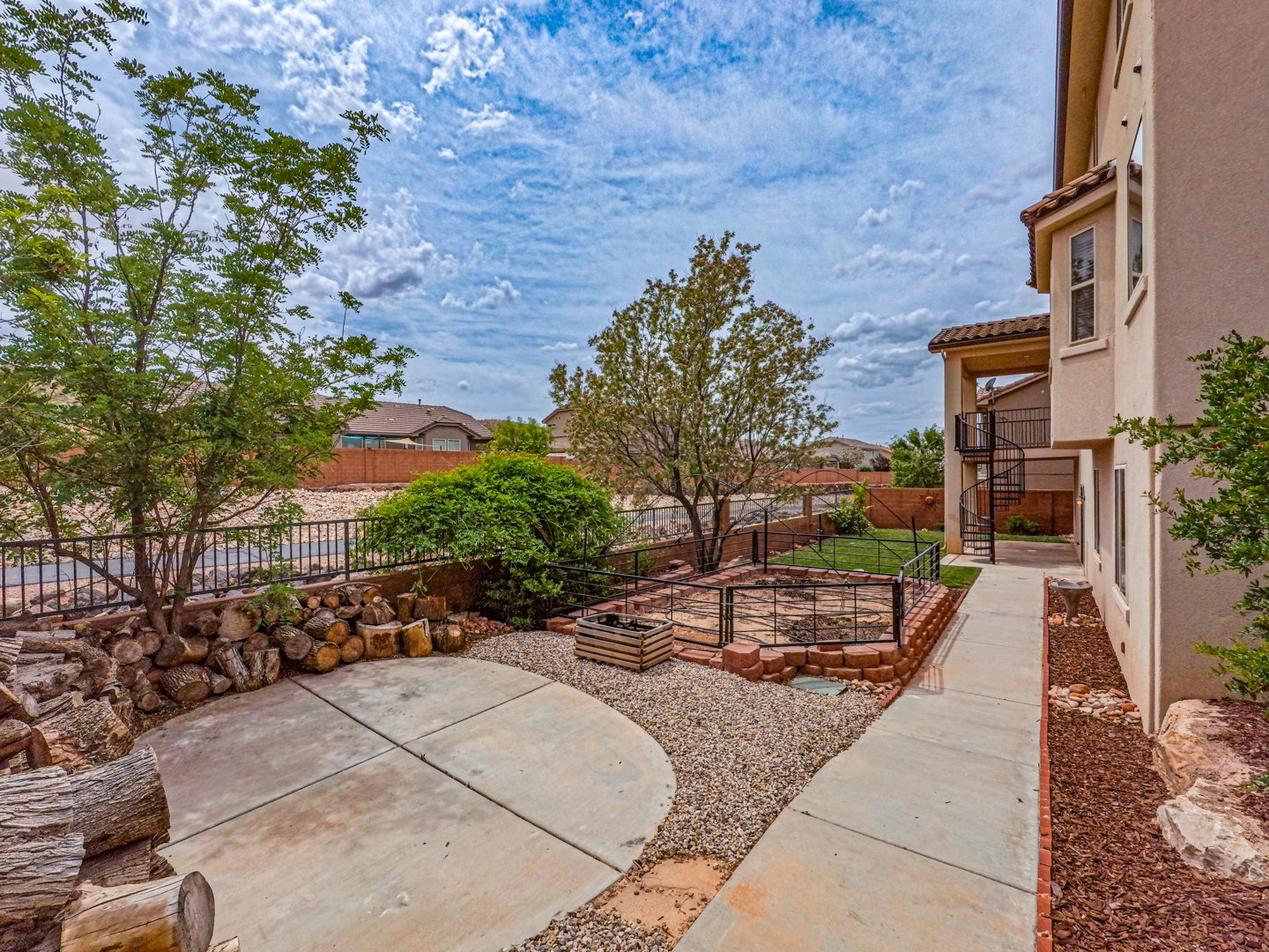 Rear exterior featuring a spiral staircase, paved walkway, and a fire pit area with stone and brick accents