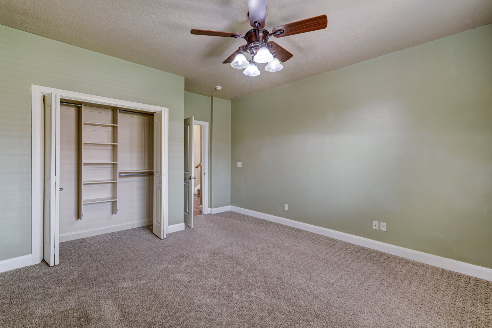 Spacious room featuring neutral wall paint, textured carpeting, and a ceiling fan with light fixture
