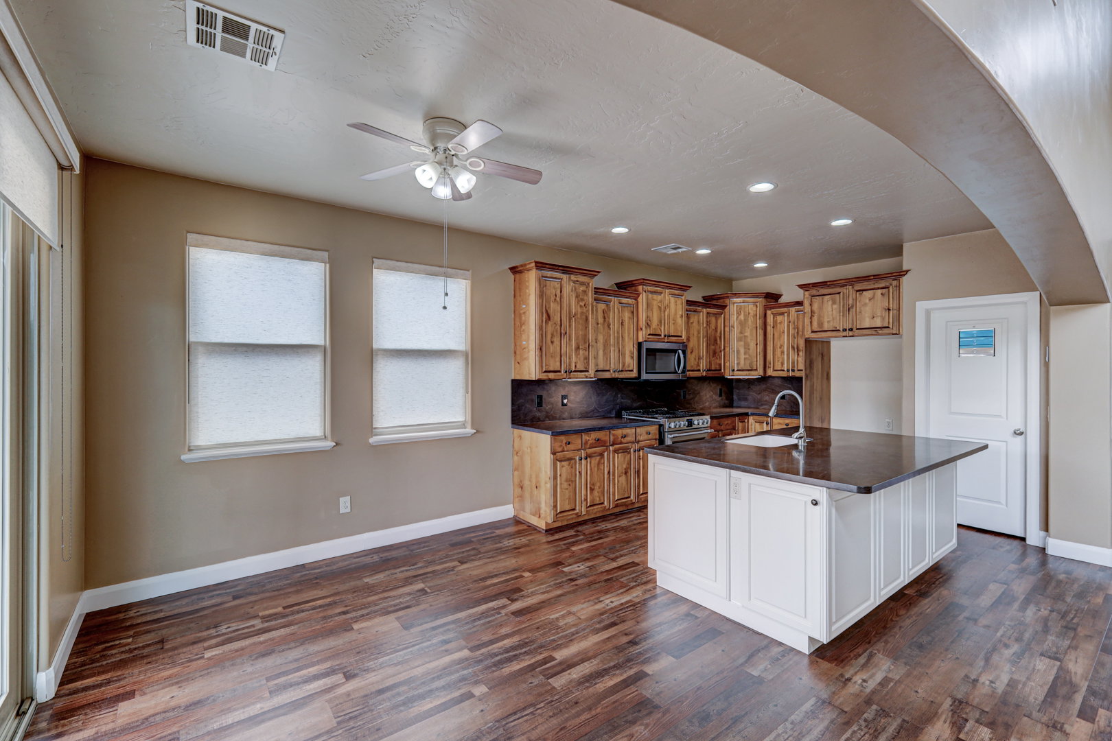 Spacious open-concept kitchen and dining area featuring wood-finish flooring, custom wood cabinetry, a central island with an integrated sink, stainless steel appliances, and recessed lighting