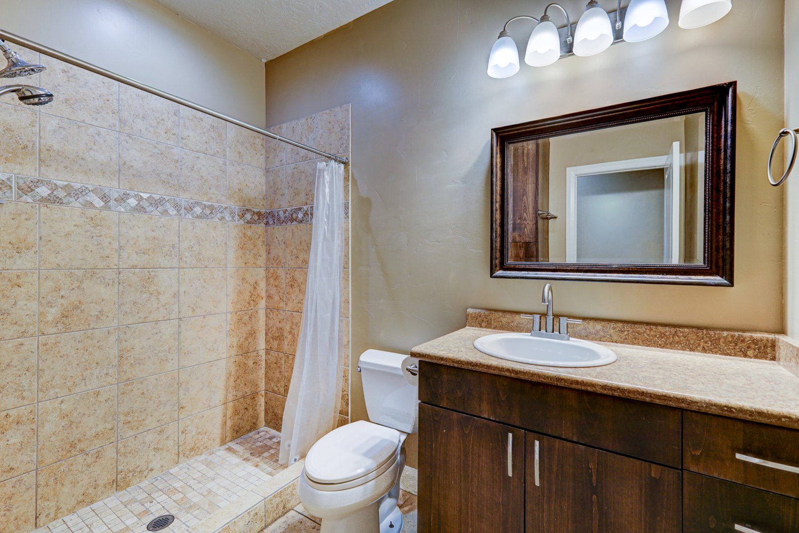Full bathroom featuring a tiled shower with decorative mosaic accent, single vanity with an oval sink, and a framed mirror