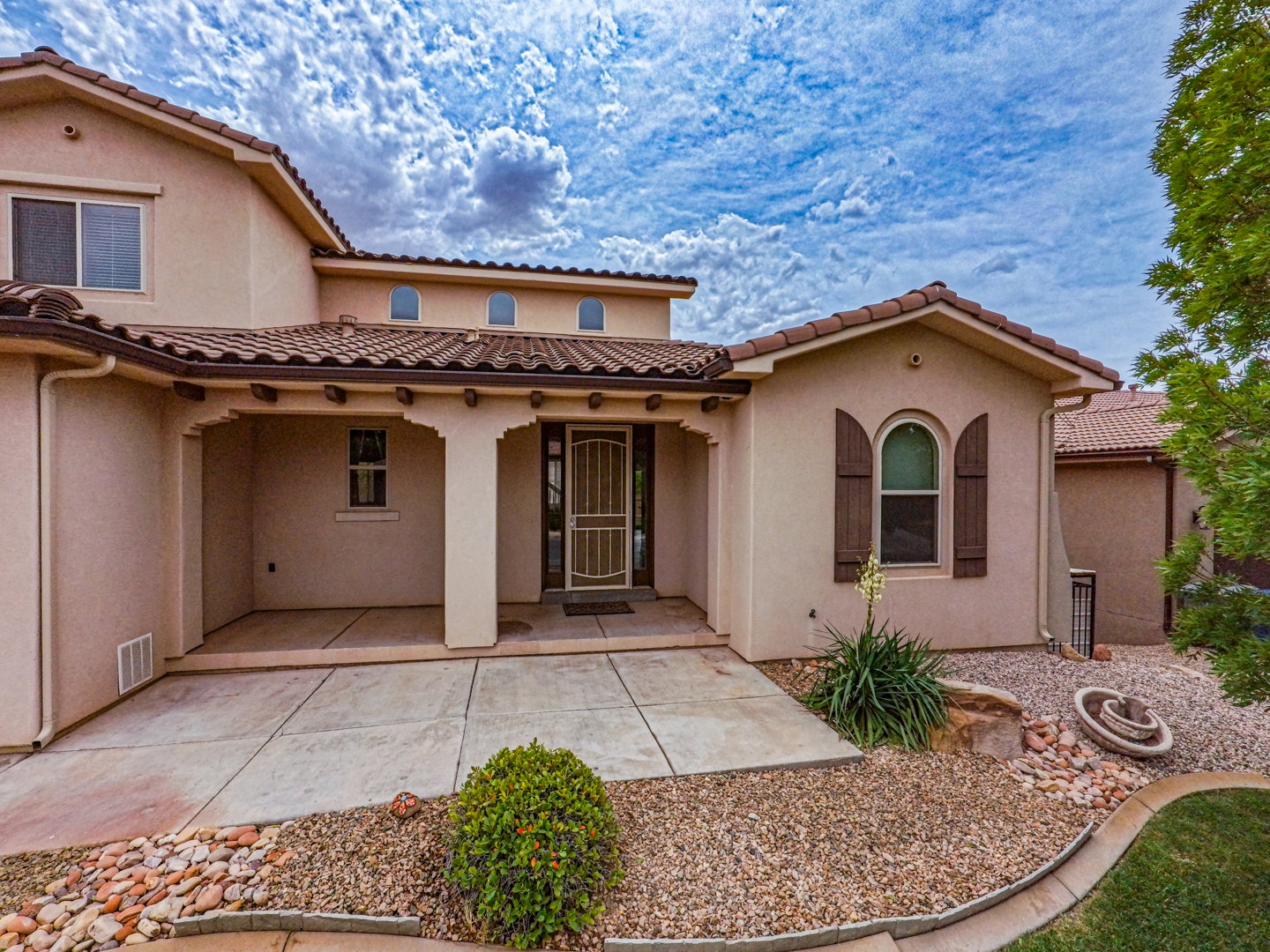 Stucco exterior featuring a covered entry, arched window with decorative shutters, and tile roof