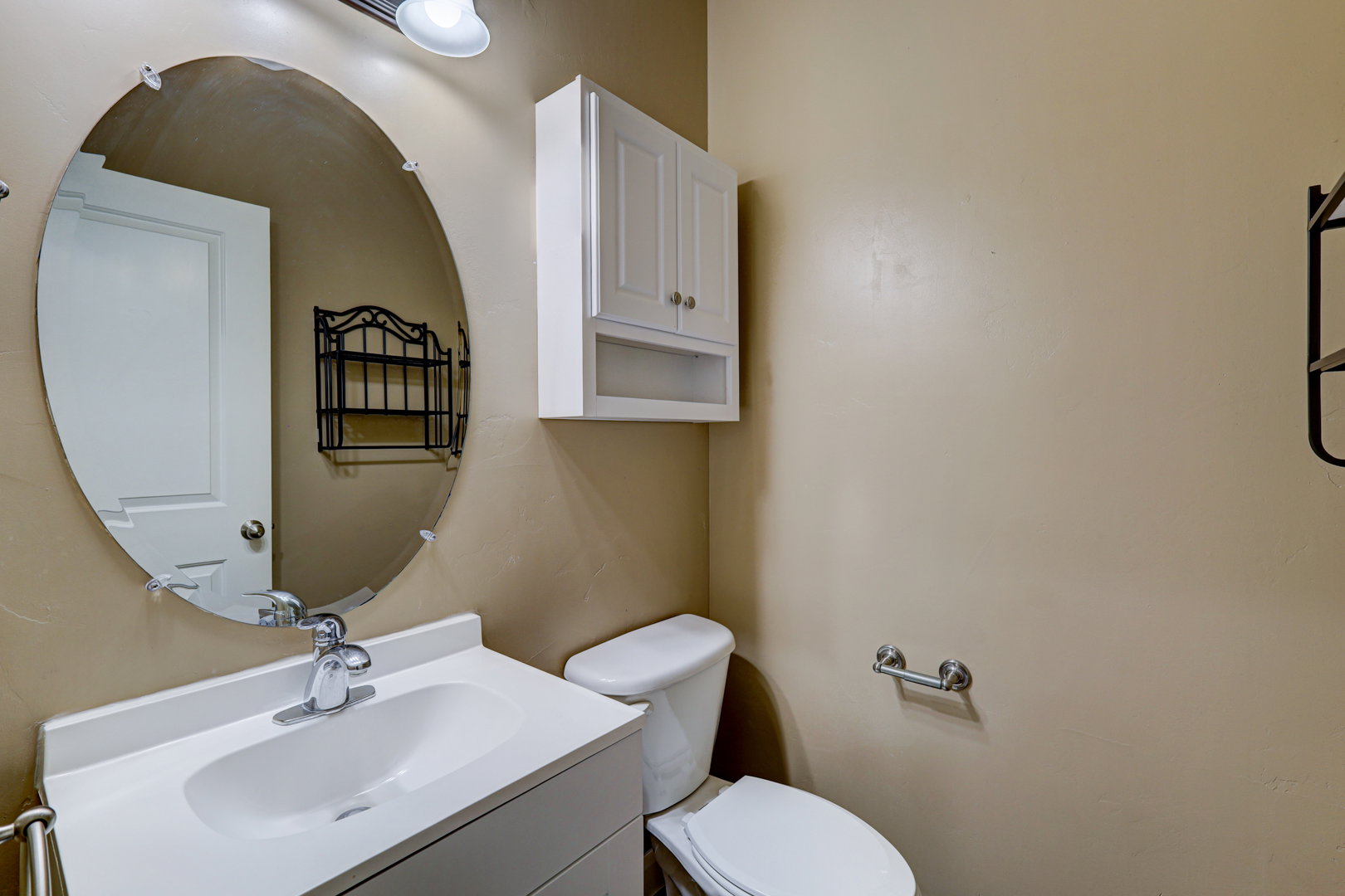 Bathroom featuring a single vanity with an integrated sink, chrome faucet, and oval mirror