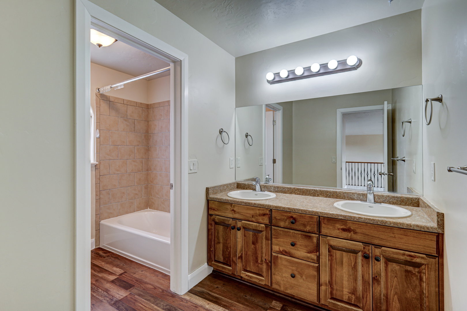 Double vanity with wood-finish cabinetry and dual undermount sinks, set under a large mirror with contemporary light fixture