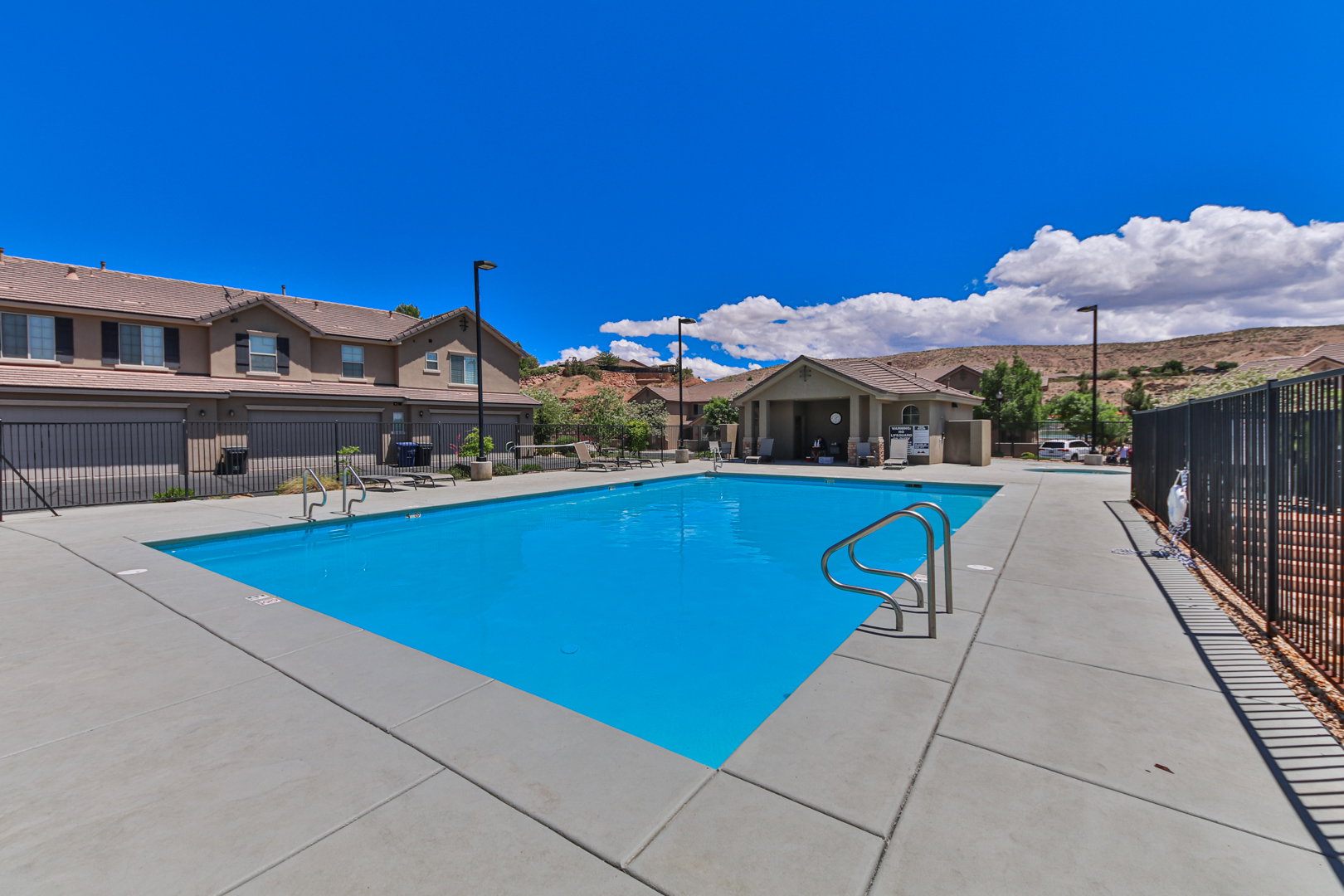 Community swimming pool with a concrete deck, metal handrails, and a nearby covered pavilion
