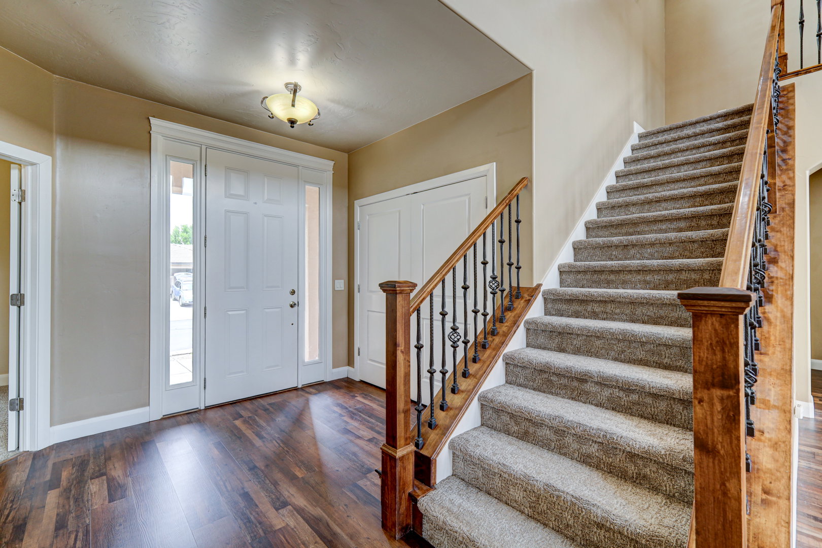 Entryway featuring wood-finish flooring and a carpeted staircase with a wood handrail and wrought iron spindles