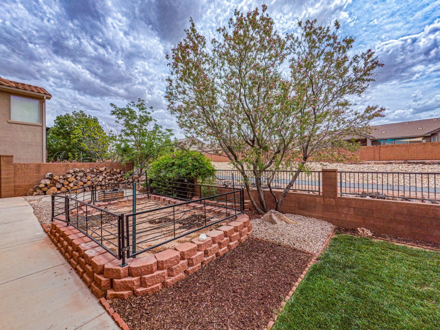 Landscaped backyard featuring a tiered retaining wall, a dedicated garden bed with metal fencing, and a mature tree