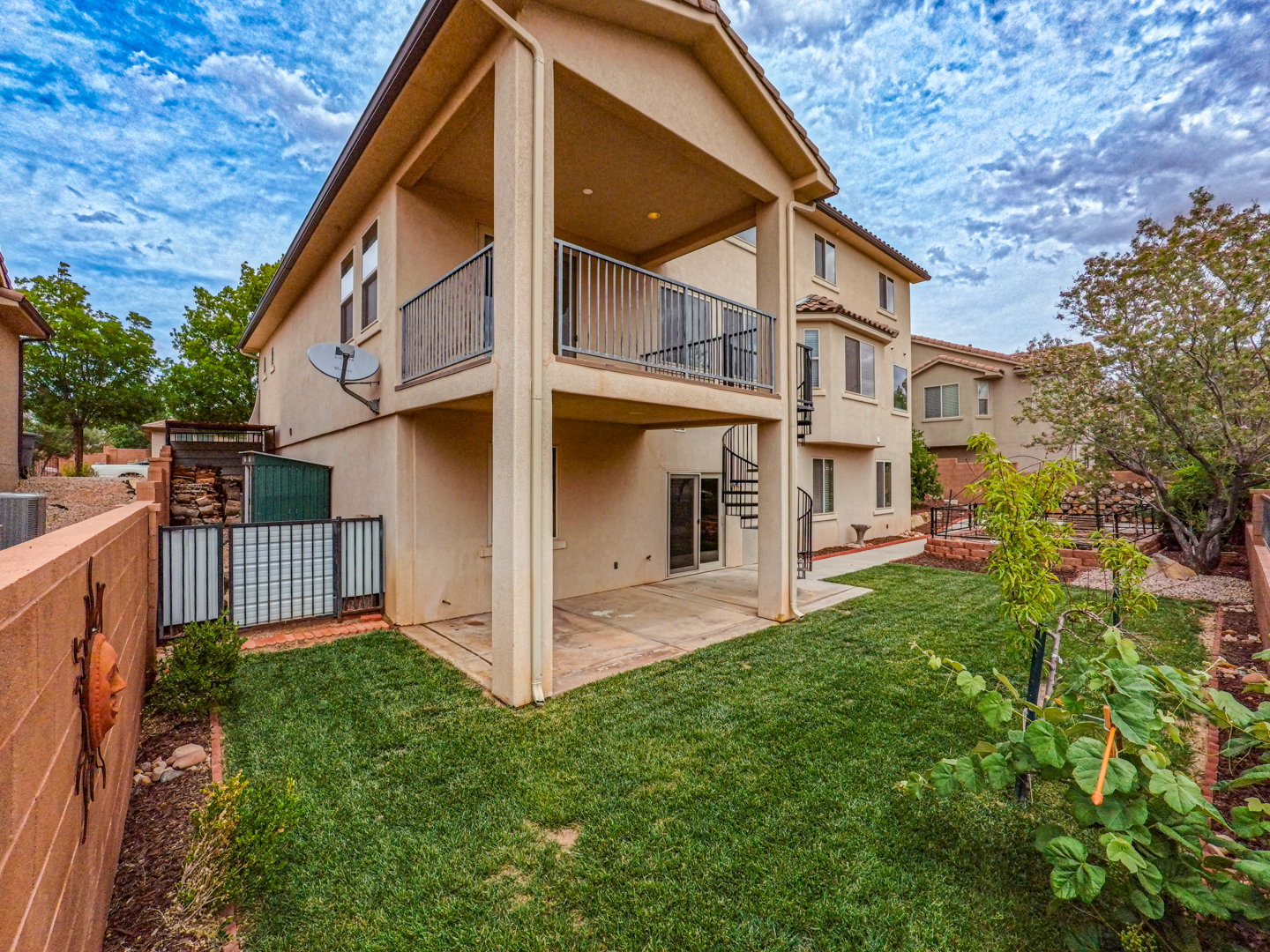 Expansive backyard featuring a manicured lawn, a covered patio, and a spiral staircase providing access to an upper-level balcony with metal railings