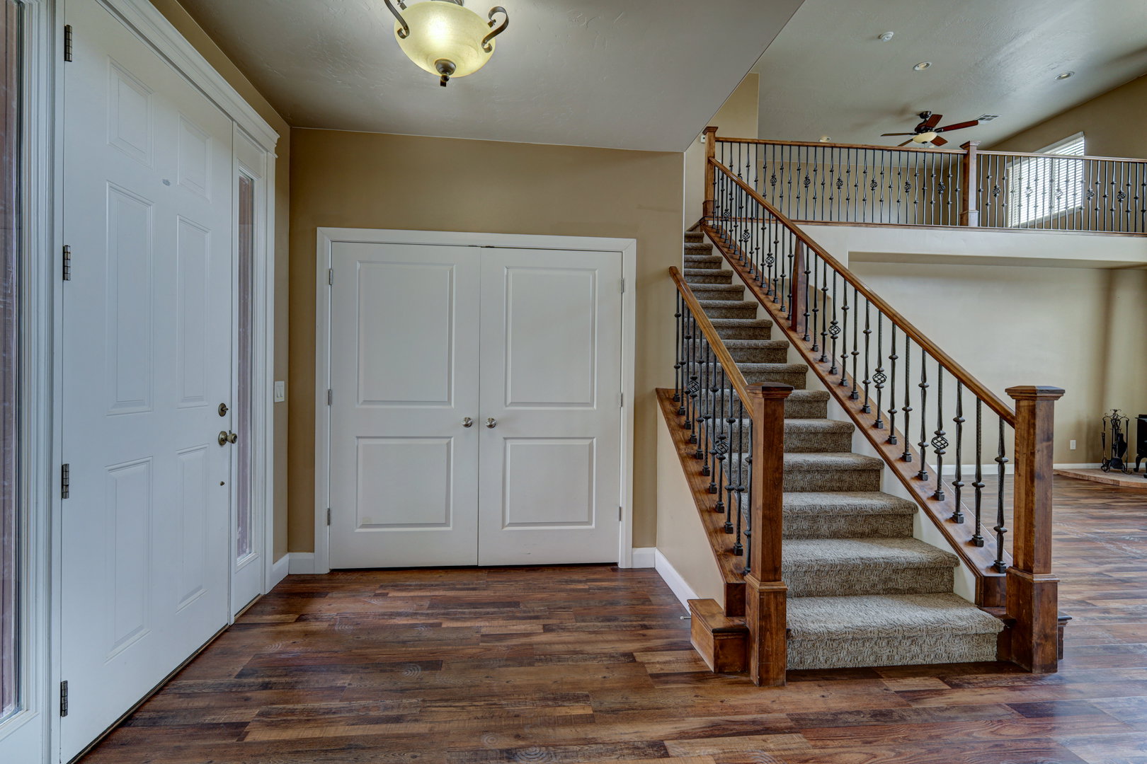 Foyer featuring wood-finish flooring, a carpeted staircase with ornate iron balusters, a wood handrail, and white panel doors