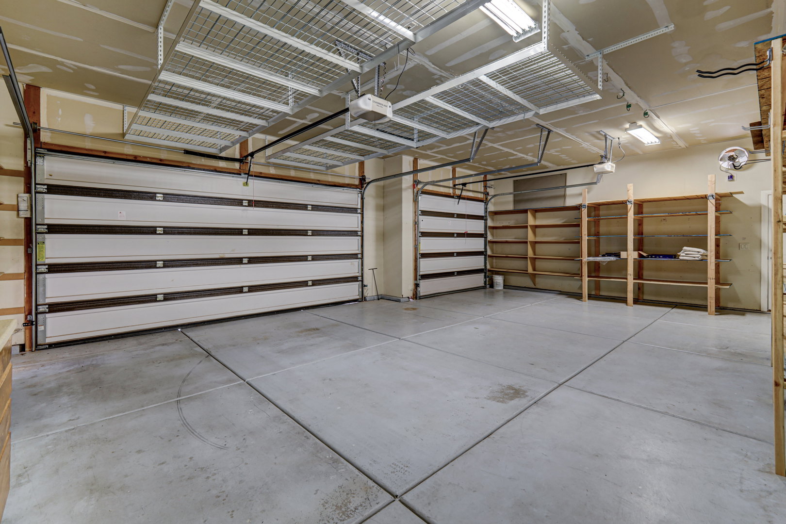 Spacious garage featuring two sectional garage doors, overhead storage racks, built-in shelving, and exposed ceiling joists