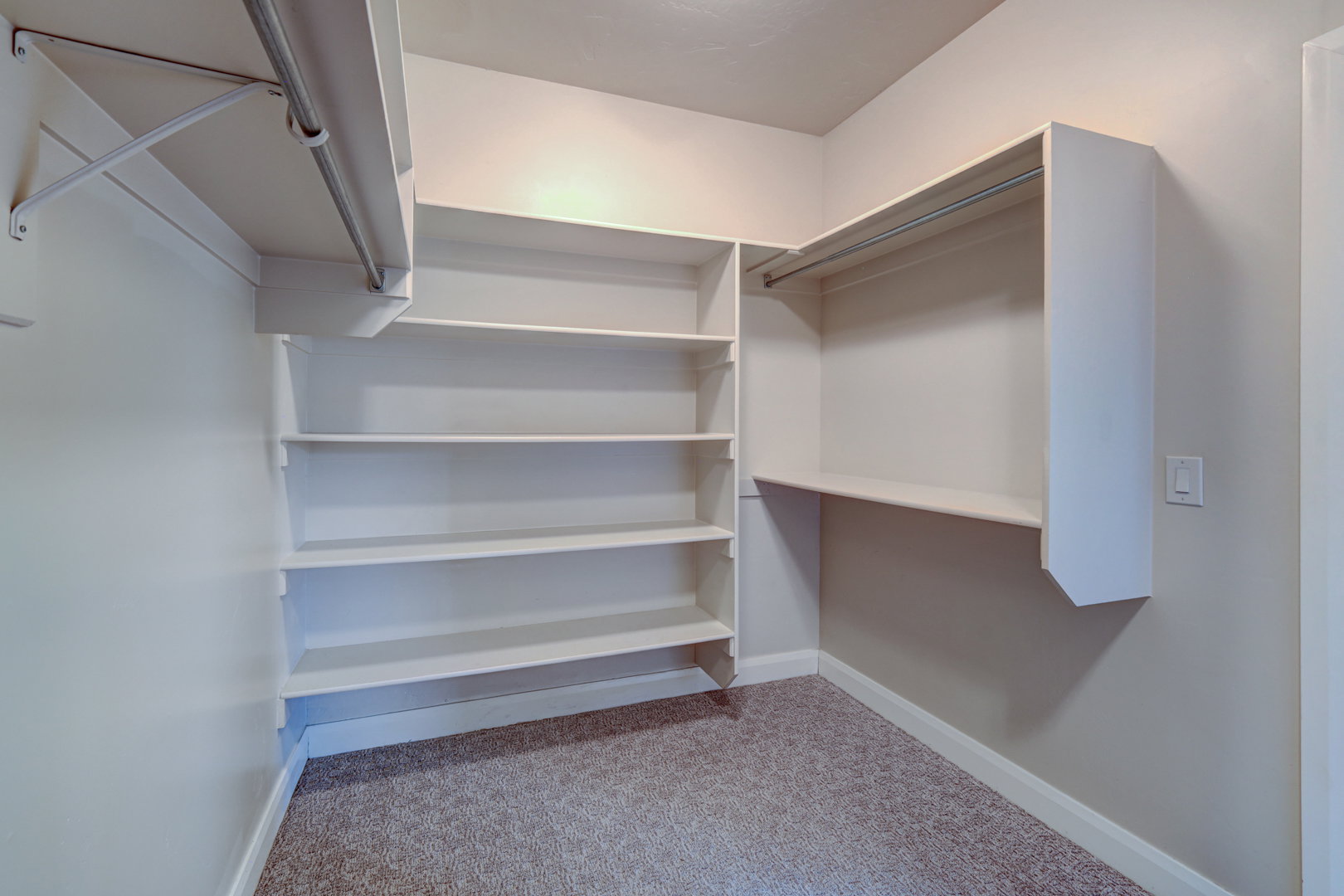 Spacious closet featuring built-in shelving, multiple hanging rods, and neutral-toned carpeting
