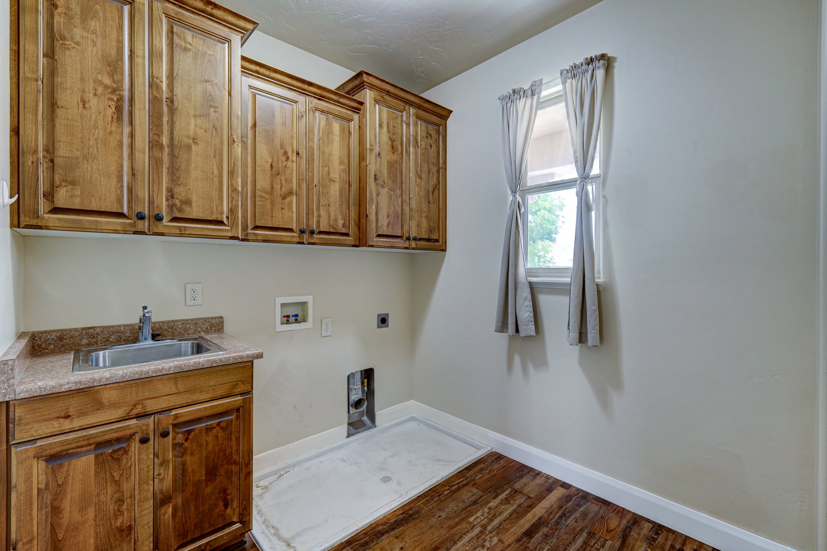 Utility space featuring extensive wood cabinetry, a built-in sink with a laminate countertop, and wood-finish flooring