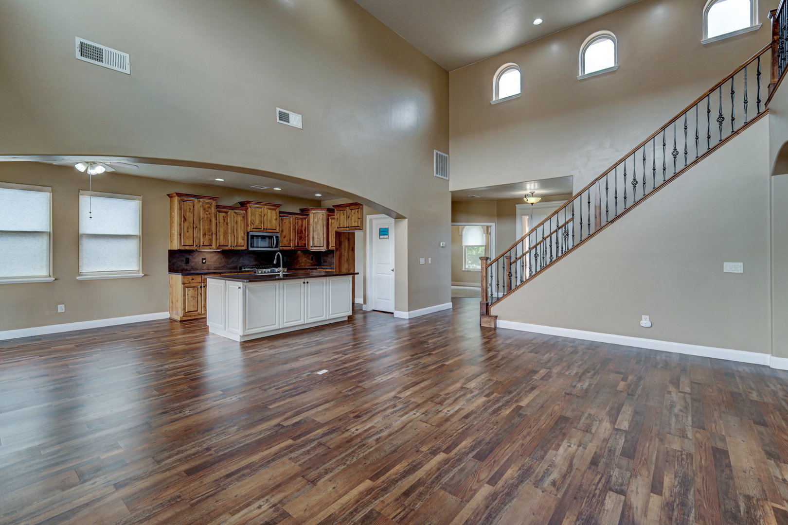 Spacious open-concept interior featuring wood-finish flooring, a two-story ceiling, and an open staircase with wrought iron balusters