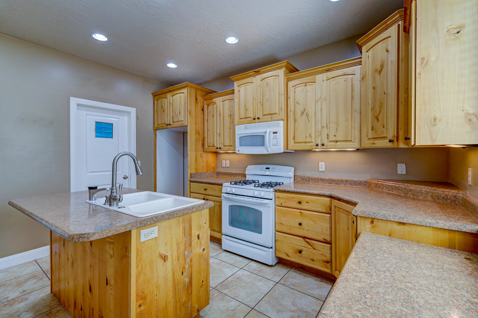 Kitchen featuring light wood cabinetry, white appliances, and a central island with an integrated sink
