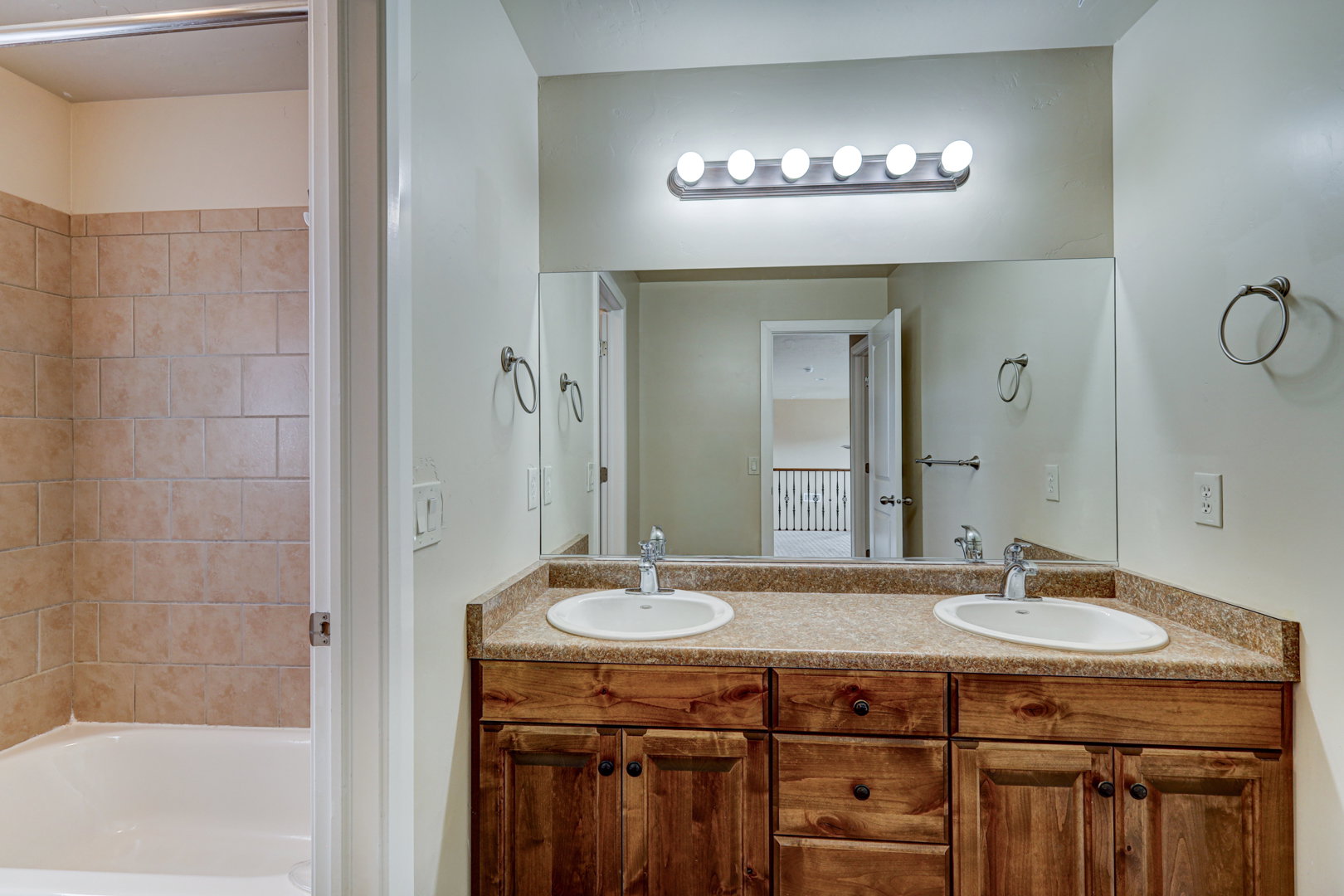 Bathroom featuring a wood-finish double vanity with dual undermount sinks, a light-toned countertop, and a large mirror with a five-light vanity fixture