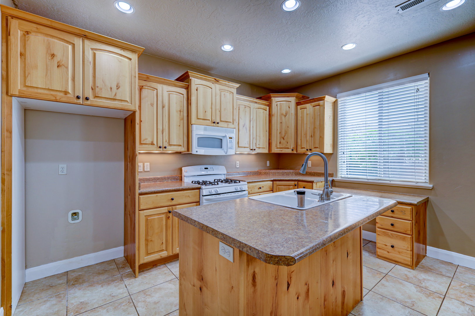 Well-appointed kitchen featuring light wood cabinetry, recessed lighting, and a center island with an integrated sink