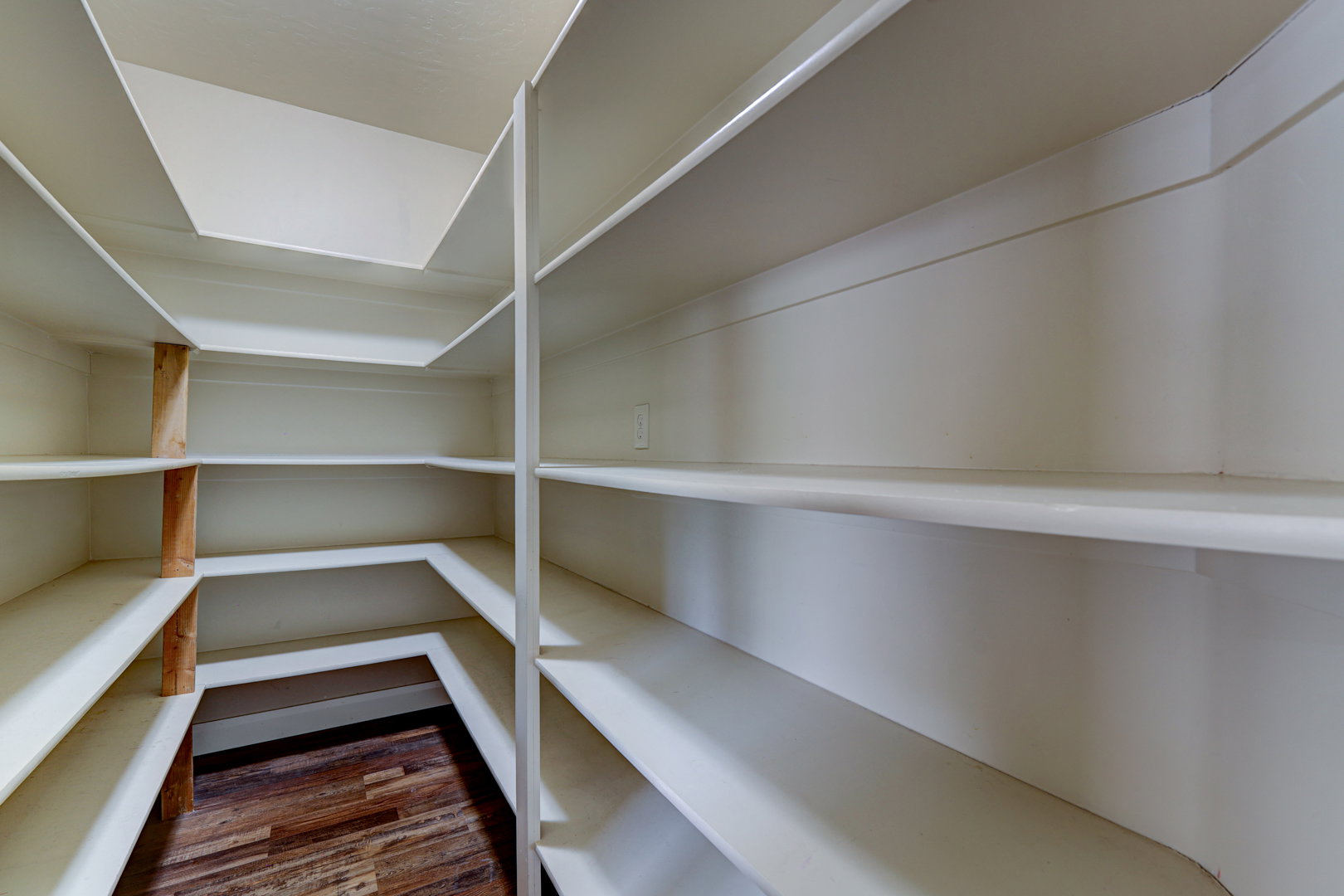 Walk-in pantry with extensive built-in shelving, white painted finishes, and wood-finish flooring