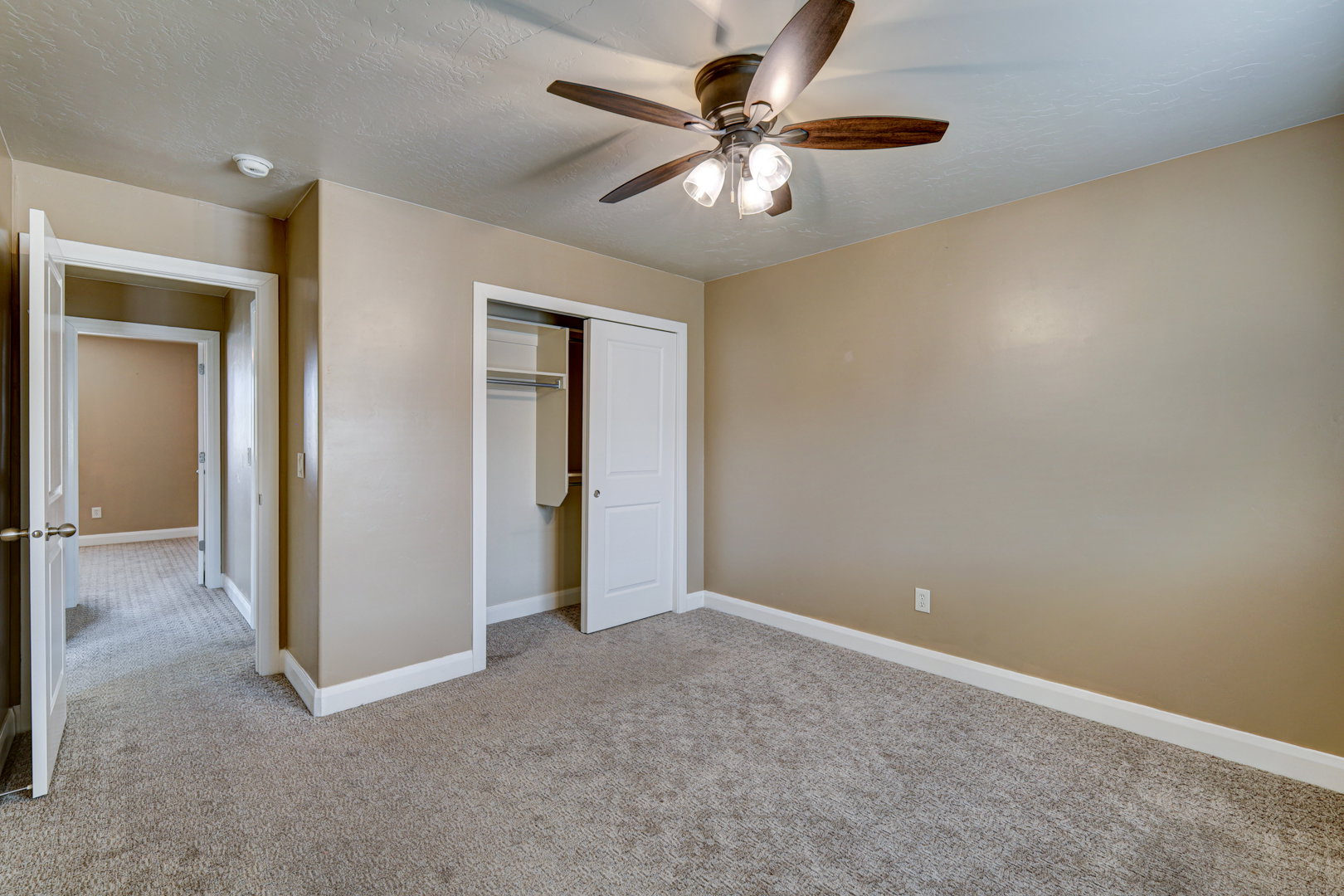 Carpeted room featuring a ceiling fan with light fixture, built-in closet with bi-fold doors, and neutral wall tones