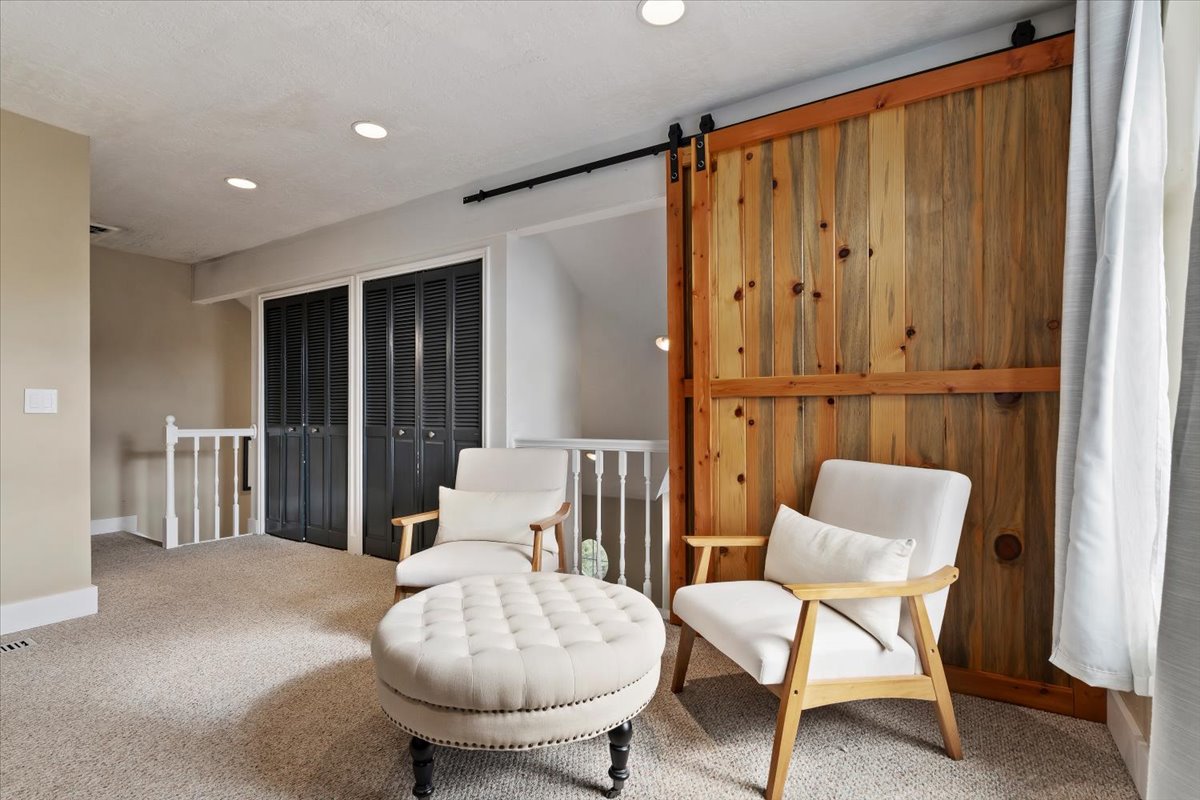 Expansive loft area featuring a natural wood barn door, recessed lighting, and soft carpeting