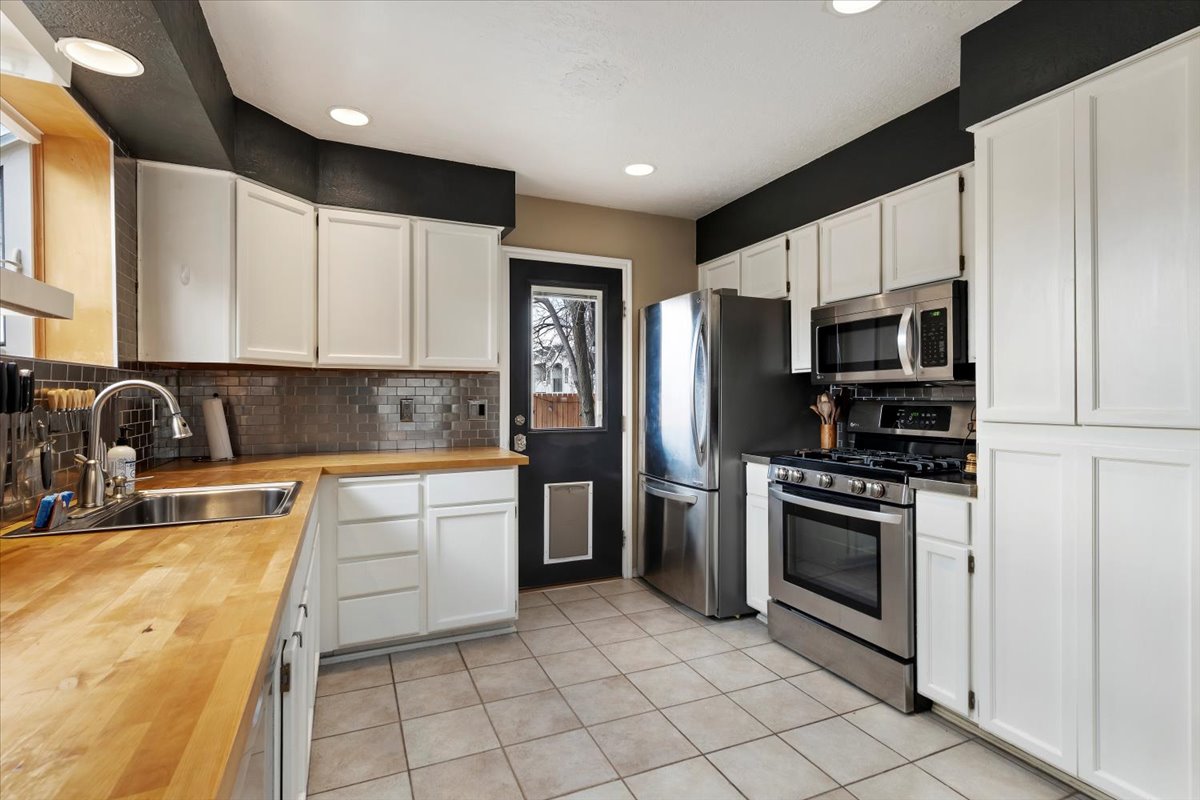 Kitchen featuring extensive white cabinetry, stainless steel appliances, butcher block countertops, a tile backsplash, and tile flooring