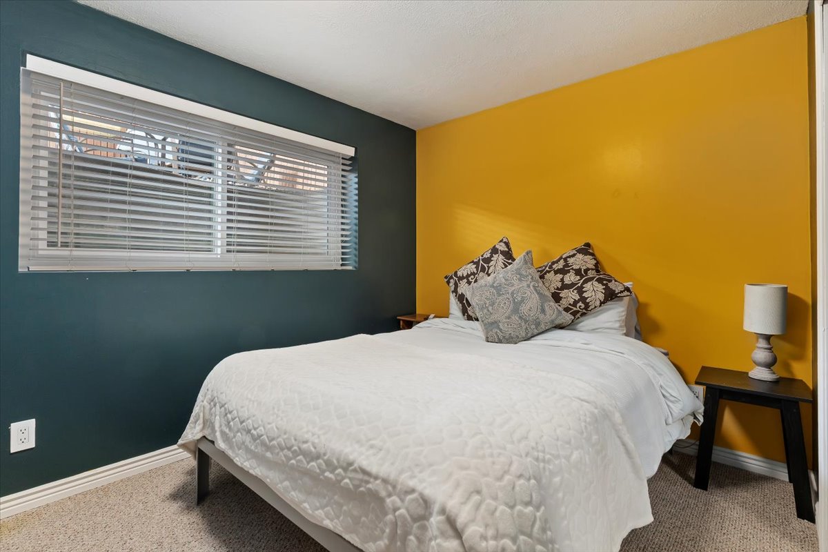 Bedroom featuring carpet flooring, crisp white baseboards, and a window with horizontal blinds