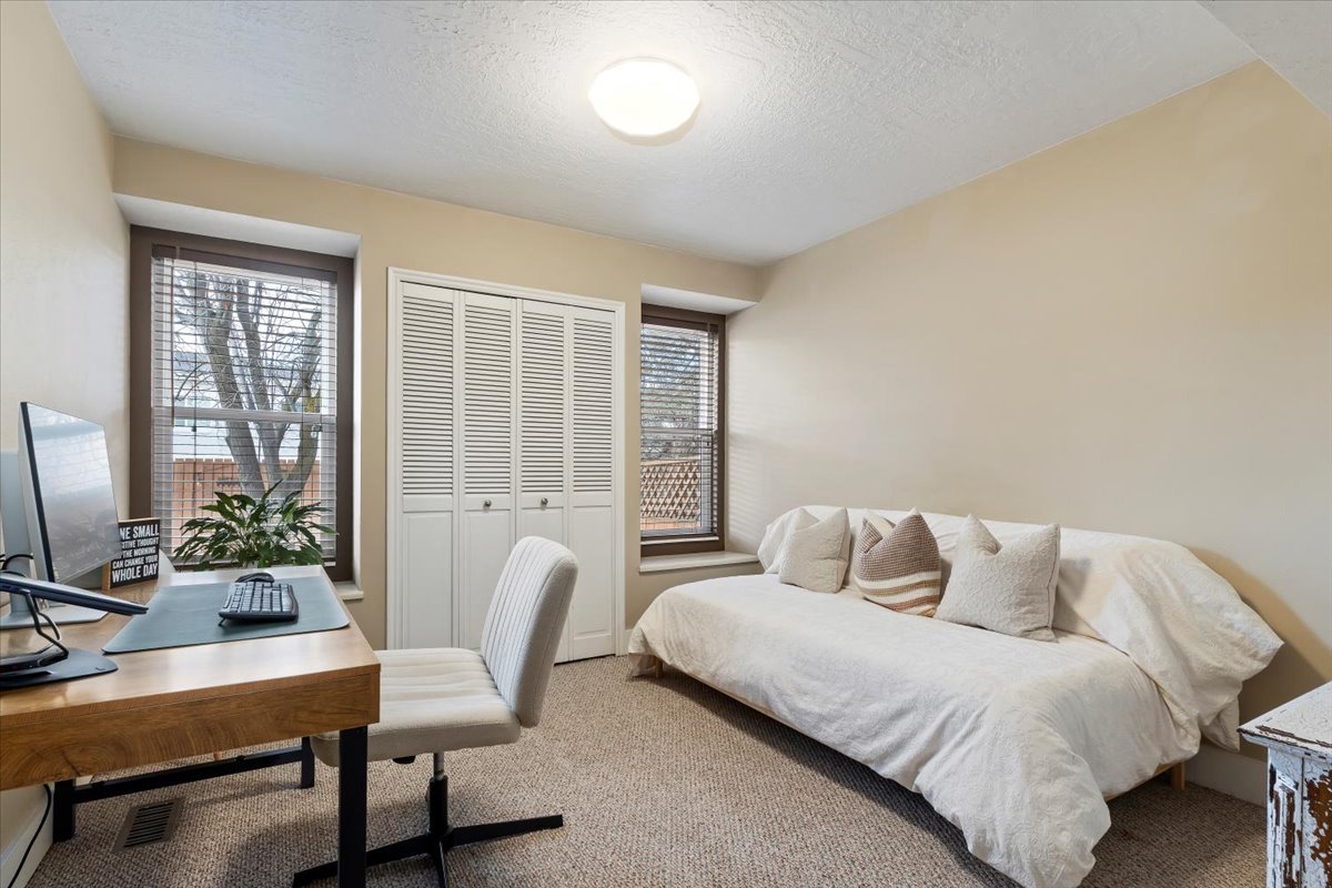 Carpeted room featuring a ceiling-mounted light fixture, two windows with blinds, and white louvered bifold closet doors