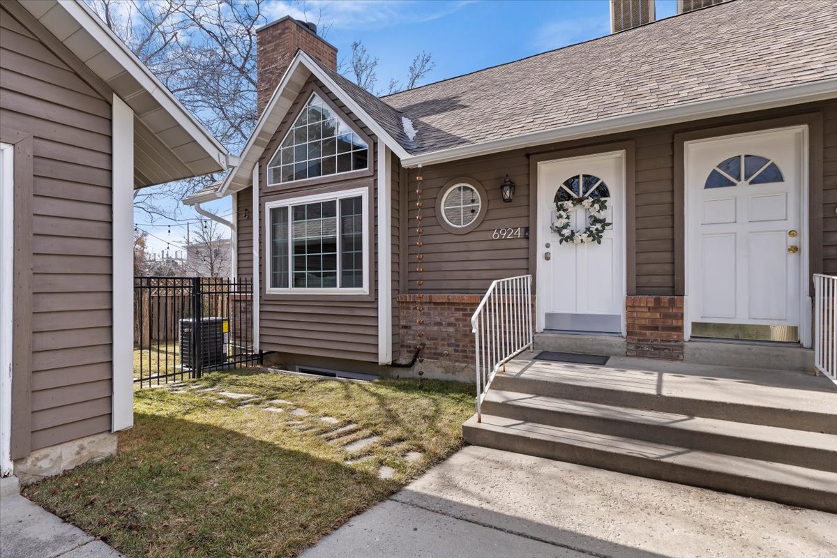 Brown siding exterior featuring a prominent gabled window, brick accents, and two white entry doors