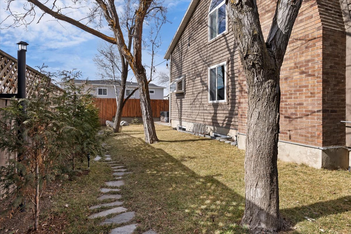 Side yard featuring a stone pathway, mature trees, manicured lawn, and privacy fencing