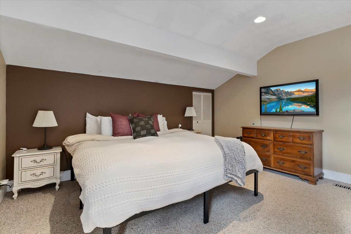 Spacious room featuring a vaulted ceiling with exposed beam, recessed lighting, brown accent wall, and light-colored wall-to-wall carpeting