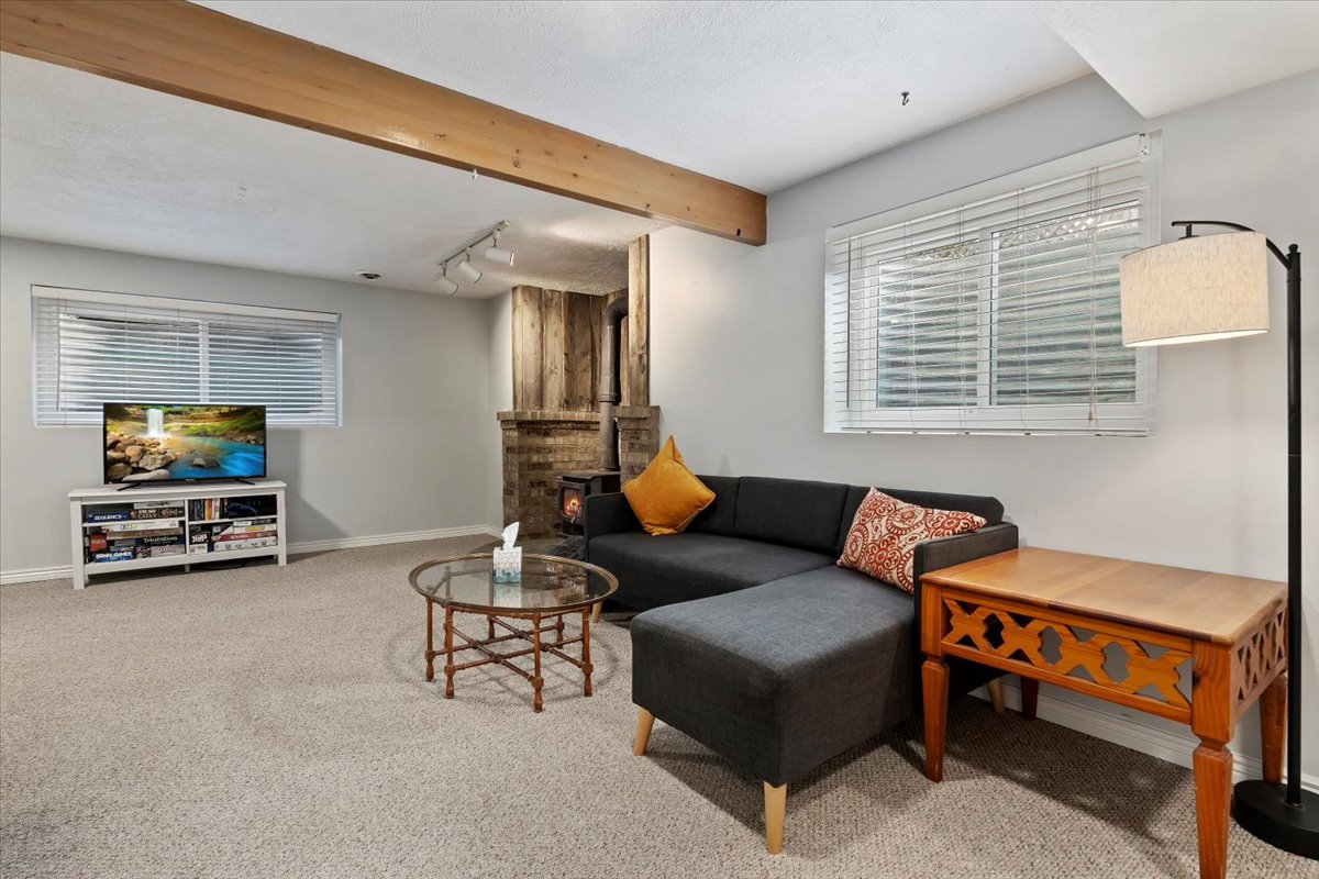 Carpeted living space featuring an exposed wood beam, recessed window with blinds, and a brick-accented wall with wood paneling