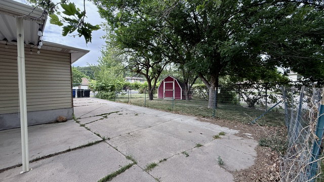Expansive concrete driveway extending towards the rear of the property, bordered by mature trees and a chain-link fence