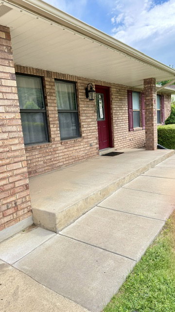 Brick exterior featuring a covered entryway with a deep red door, black exterior sconce lighting, and matching red louvered shutters