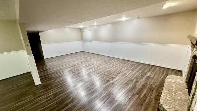 Spacious room with wood-finish flooring, recessed lighting, white wainscoting, and a brick fireplace