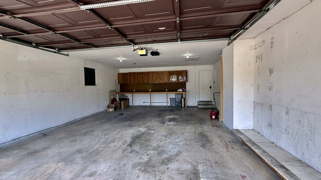 Spacious garage featuring a brown overhead door, a built-in workbench with storage cabinetry, and a service door
