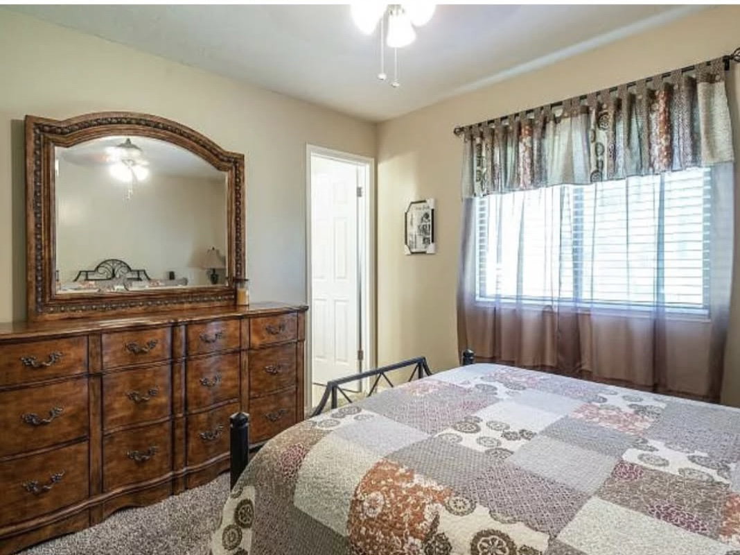 Room featuring a ceiling fan, a window with horizontal blinds and curtains, and a door