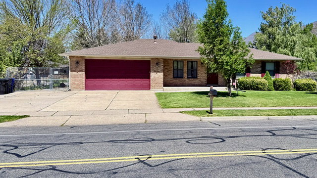 Ranch-style exterior with brick facade, a two-car garage with a red door, and a brown shingle roof