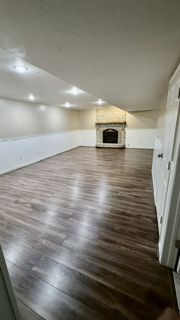 Spacious room featuring wood-finish flooring, a brick fireplace with a stone mantel, recessed lighting, and white baseboards
