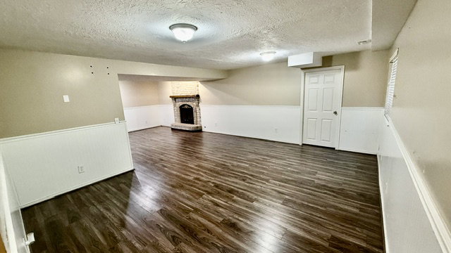 Spacious room featuring wood-finish flooring, wainscoting, and a stone fireplace