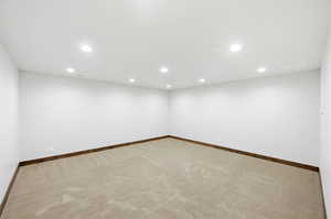 Spacious room with white walls, recessed ceiling lighting, light-toned carpet flooring, and dark wood-finish baseboards