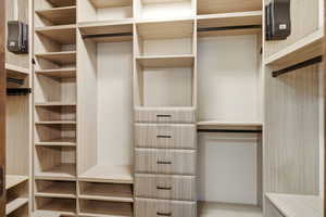 Custom closet system featuring light wood-finish shelving, integrated drawers with dark hardware, multiple hanging rods, and varied storage compartments