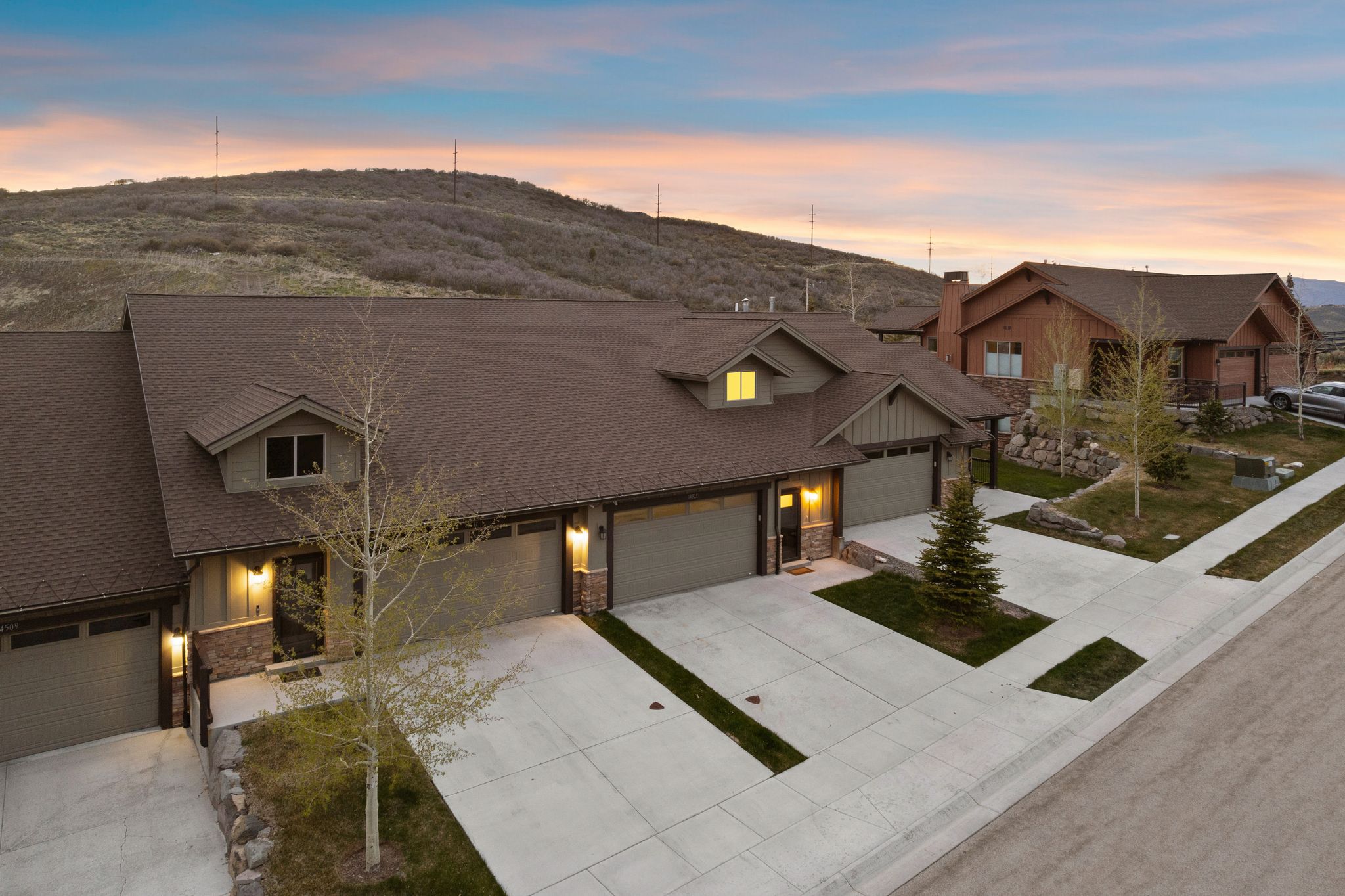 Townhome exterior featuring earth-toned siding, stone accents, multiple attached garages, concrete driveways, and mature landscaping