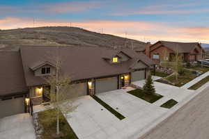 Townhome exterior featuring earth-toned siding, stone accents, multiple attached garages, concrete driveways, and mature landscaping