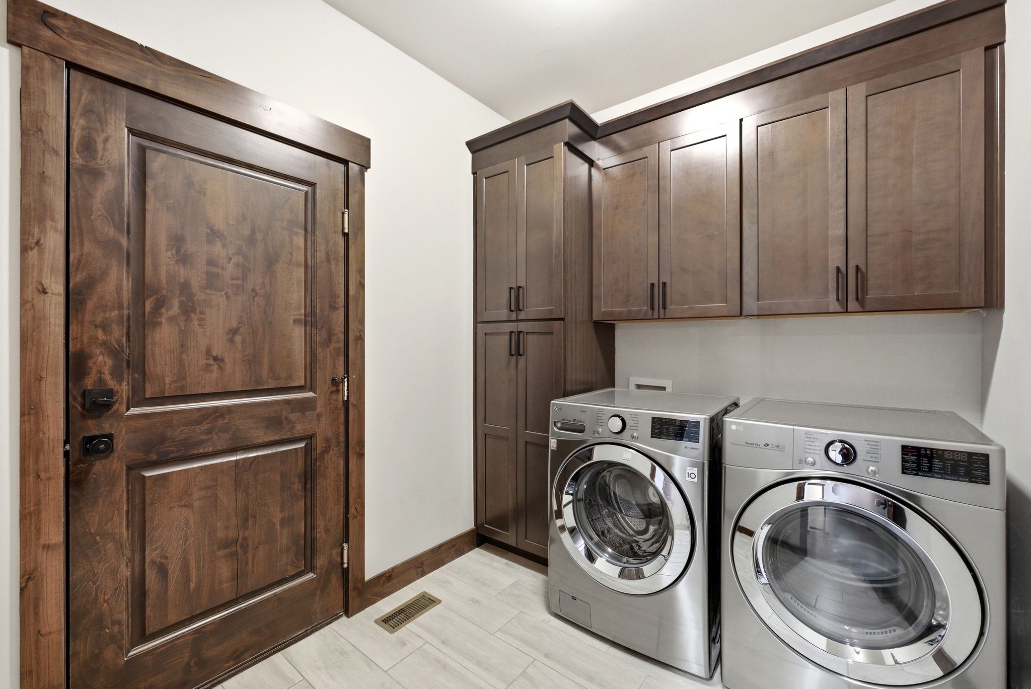 Dedicated laundry area featuring wood-finish cabinetry, a tall storage pantry, and light-toned tile flooring