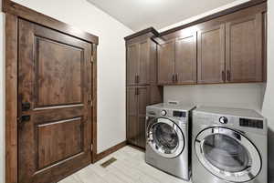 Dedicated laundry area featuring wood-finish cabinetry, a tall storage pantry, and light-toned tile flooring