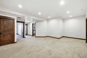 Spacious interior room featuring light-toned carpet flooring, recessed ceiling lighting, and crisp white walls